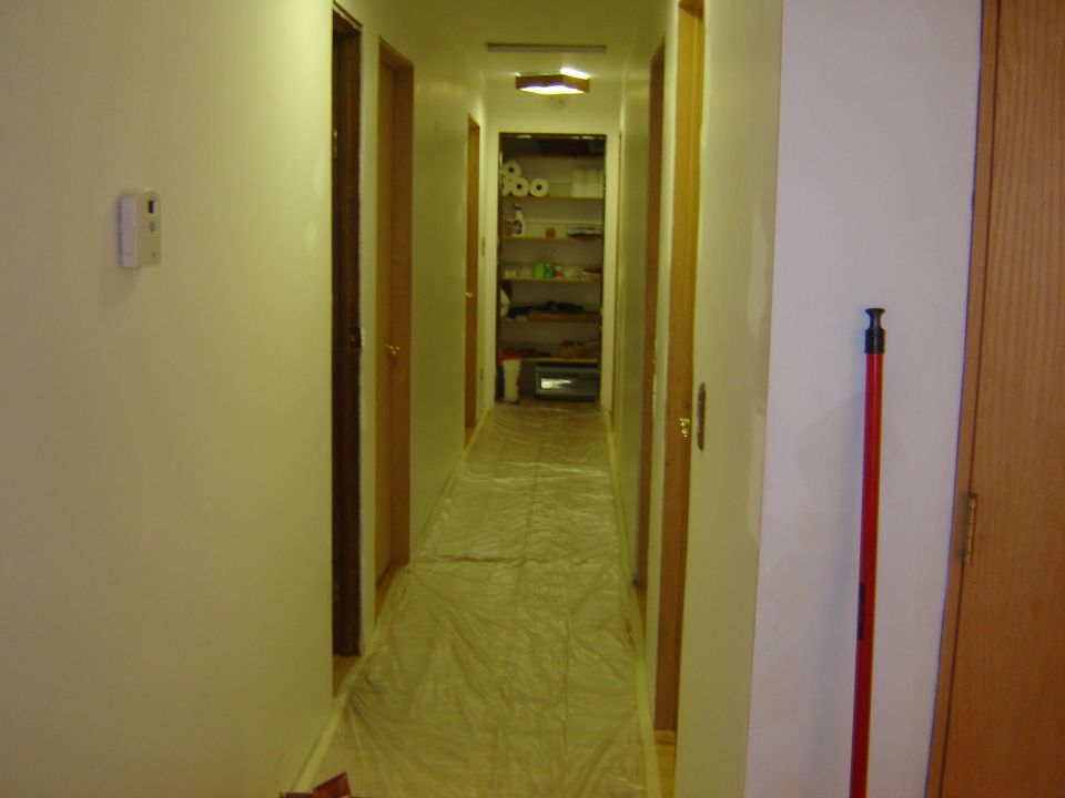 Hallway with plastic sheeting on the floor and shelves stocked with items in the background
