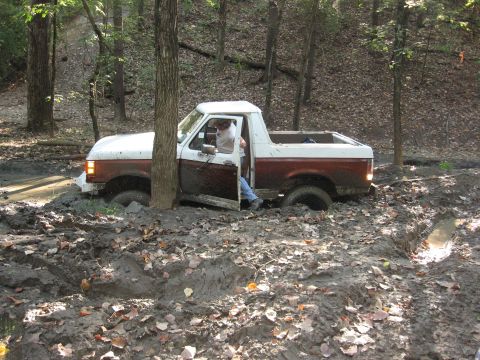 1987 Jeep Comanche - A two-tone pickup truck is stuck in thick mud with its driver's door open.