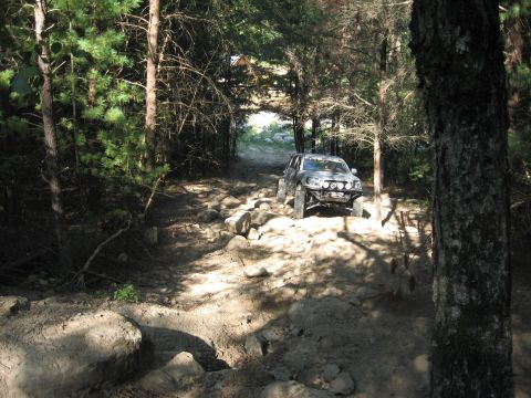 1987 Jeep Comanche - An off-road vehicle tackles a challenging rocky path through a dense forest.