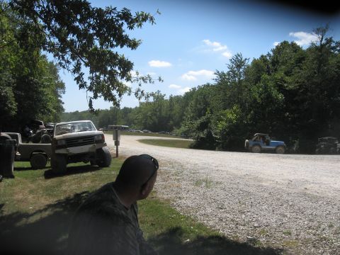 1987 Jeep Comanche - Several off-road vehicles are parked and driving on a dirt road in a wooded area.