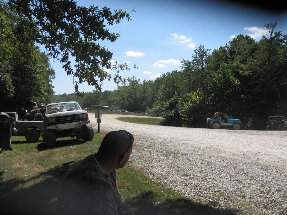 White pickup truck and blue Jeep on a dirt road with trees and sky