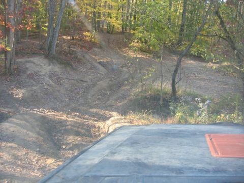 1987 Jeep Comanche - Navigating a dirt trail through a wooded area, with a portion of a vehicle visible at the bottom of the frame.
