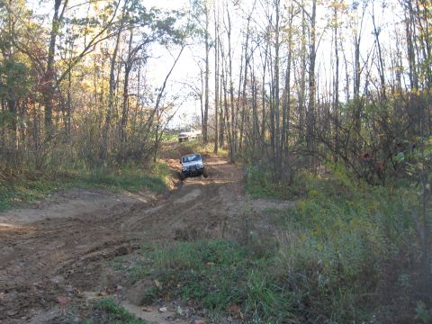 1987 Jeep Comanche - Two SUVs navigate a muddy, wooded trail during an off-road excursion.