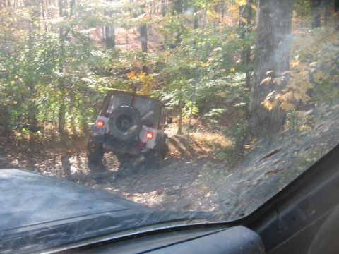 1987 Jeep Comanche - A Jeep Wrangler navigates a wooded trail, viewed from another vehicle.