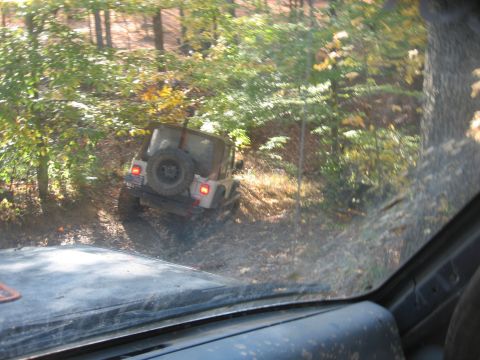 1987 Jeep Comanche - A white Jeep Wrangler navigates a wooded trail, with another vehicle visible in the foreground.