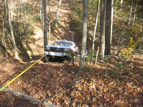 1987 Jeep Comanche - A white pickup truck is being pulled by a yellow tow strap through a wooded area covered in fallen leaves.