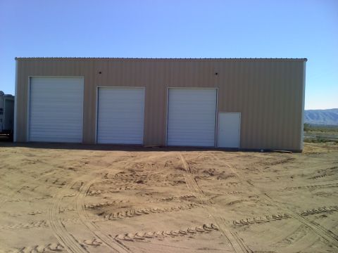 2011 Ford F-250 - A large tan building with multiple garage doors sits in a dusty lot under a clear blue sky.