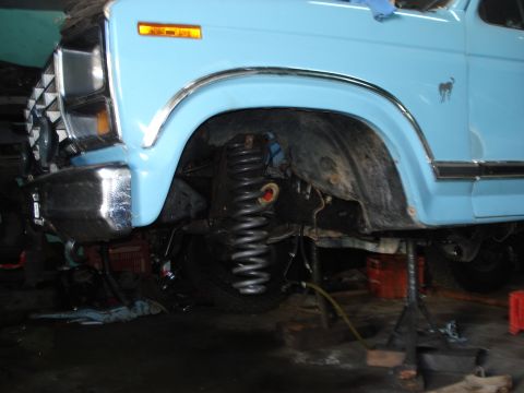 1980 Ford Bronco - The front fender and grille of a light blue SUV are visible, with the front suspension system exposed for maintenance.