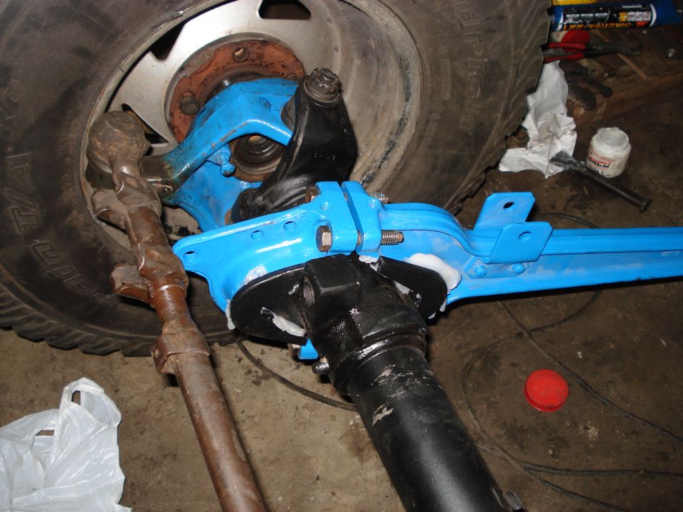 Close-up of a blue-painted front axle assembly with a tire and steering linkage components