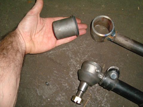 1980 Ford Bronco - Close-up of automotive suspension components, including a bushing and tie rod ends, on a workshop floor.