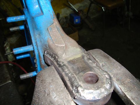 1980 Ford Bronco - A close-up view of a blue painted metal component, secured in a vise and showing signs of repair with welding.