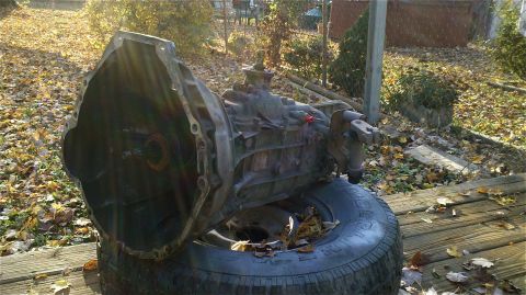 1995 Ford F-150 - Transmission assembly sits on a tire on a wooden deck, surrounded by autumn leaves.