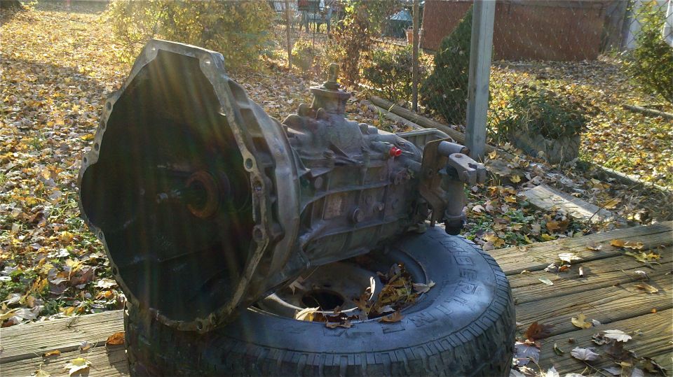 Transmission assembly resting on a tire outdoors, with fallen leaves scattered around