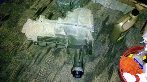 1995 Ford F-150 - A used transfer case sits on a weathered wooden floor, next to cleaning supplies and a bottle of fluid.