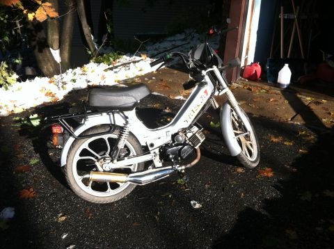 1999 Tomos Targa - A moped is parked on a wet surface near a garage, with fallen leaves and a dusting of snow visible.