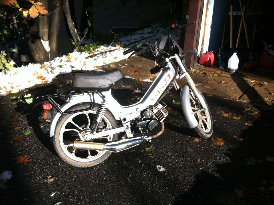 White Tomos Targa moped with chrome expansion exhaust on a leaf-covered driveway