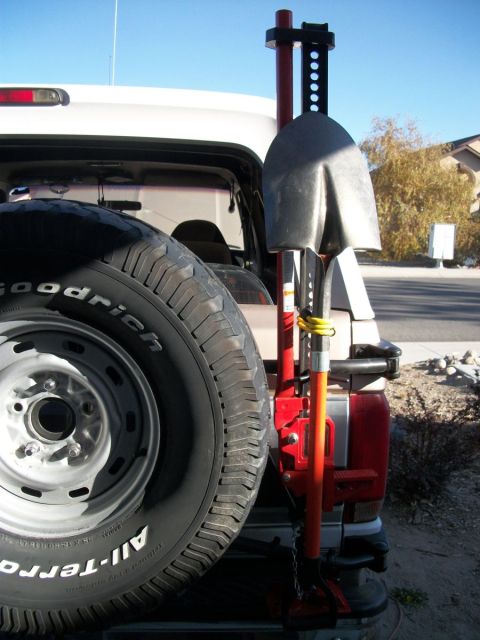 1996 Ford Bronco - Spare tire and recovery gear, including a shovel and Hi-Lift jack, are mounted on the rear of a white SUV.