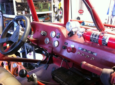 Suzuki Samurai - Interior of a red-painted rock crawler in a garage, showing the flat metal dash with a cluster of Auto Meter gauges, a red START button, an…