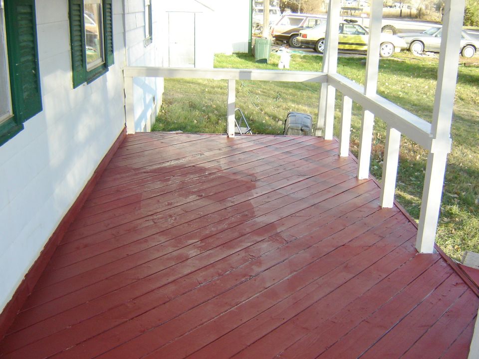 Red painted wooden porch with white railing, and two cars parked in the background