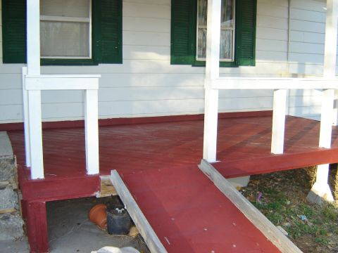 1984 Ford Mustang - A red painted porch features white railings and a wooden ramp leading up to the entrance.