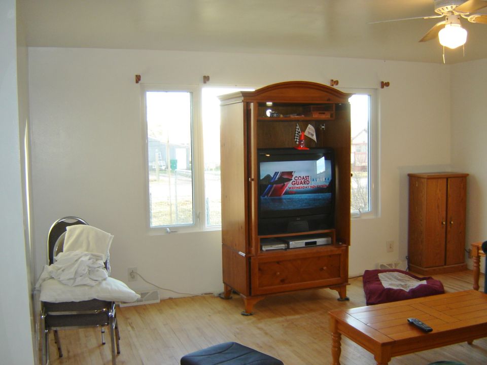 Living room interior with a wooden entertainment center holding a TV, a coffee table, and a chair with clothes