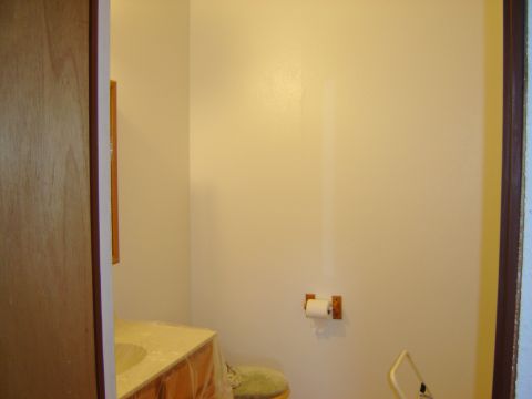 1984 Ford Mustang - A partially renovated bathroom shows a sink vanity covered in plastic sheeting and a toilet with a roll of toilet paper nearby.