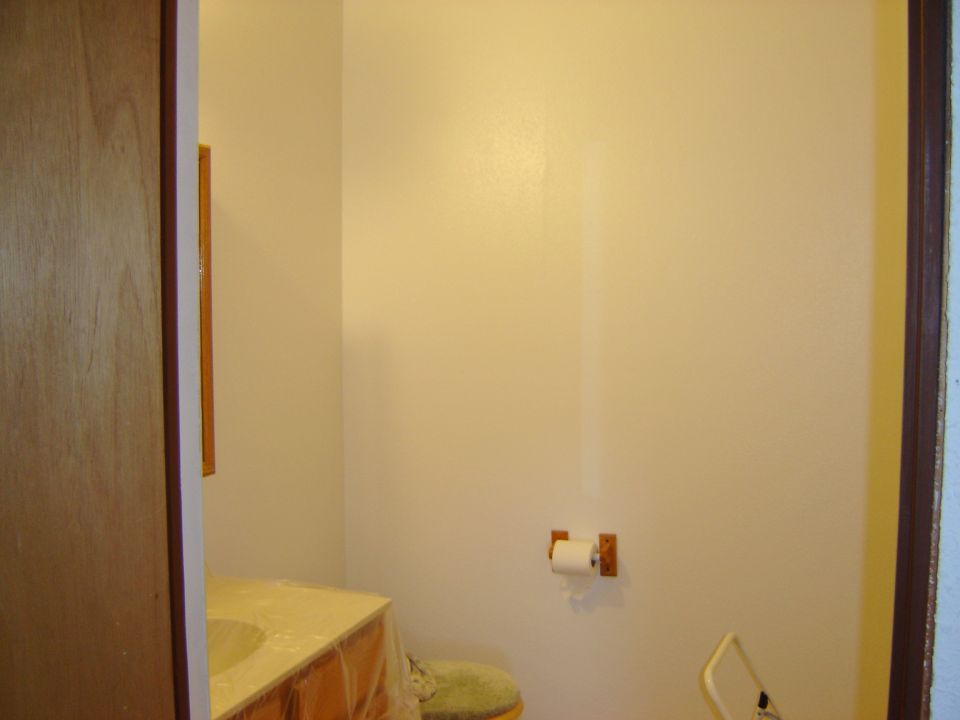 Bathroom with a sink vanity covered in plastic, a toilet, and a roll of toilet paper on the wall
