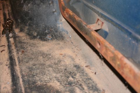 1989 Ford Bronco - The interior floor of a vehicle shows signs of wear and tear, with a rusty metal trim piece and accumulated dirt.