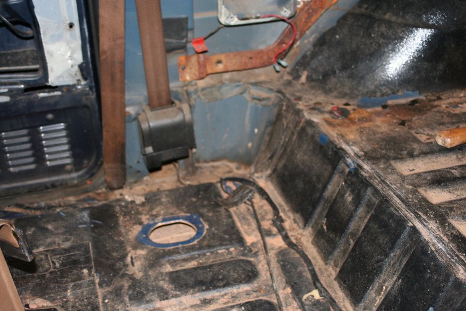 Interior floor and seatbelt mechanism of a vehicle, showing rust and dirt