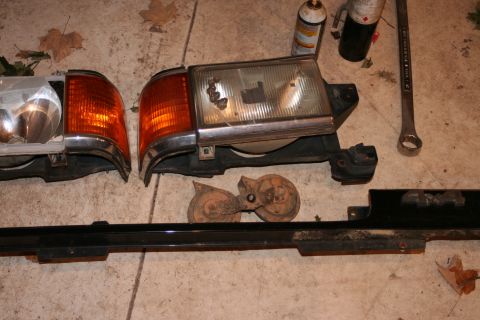 1989 Ford Bronco - Disassembled car parts lie on a concrete surface, including headlights, turn signals, and horns.