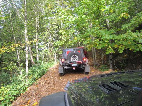 2008 Jeep Wrangler - Two Jeep Wranglers navigate a rocky, wooded trail during an off-road excursion.