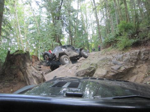 2008 Jeep Wrangler - Two Jeeps navigate a challenging off-road course through a dense forest with steep inclines and large rocks.