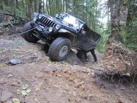 2008 Jeep Wrangler - A black Jeep Wrangler tackles a challenging, steep, and rocky off-road course in a wooded area.