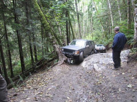 2008 Jeep Wrangler - Two SUVs navigate a challenging, muddy trail through a dense forest.