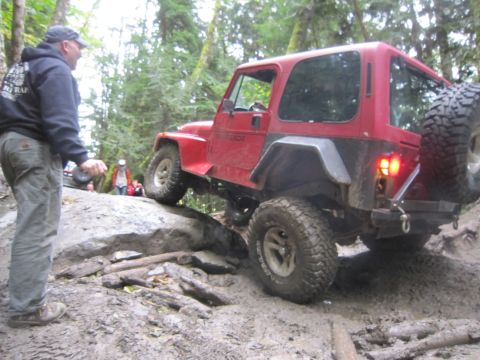 2008 Jeep Wrangler - A red Jeep Wrangler is shown tackling a difficult off-road course with a person observing the maneuver.