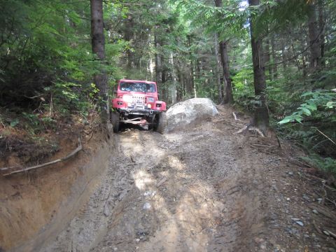 2008 Jeep Wrangler - Red Jeep Wrangler navigates a challenging muddy trail through a dense forest.