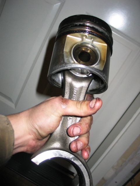 1984 Ford Bronco - A hand holds a used piston and connecting rod assembly, likely from an engine rebuild or repair.