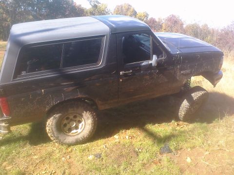 1995 Ford Bronco - This black 1995 Ford Bronco is shown in a three-quarter front view, highlighting its lifted suspension and off-road tires.