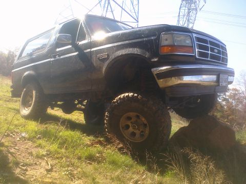 1995 Ford Bronco - This black 1995 Ford Bronco is shown navigating a rocky, grassy terrain with its lifted suspension.