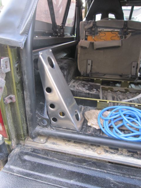 1974 Ford Bronco - The interior of a green vehicle reveals a metal bracket, a folded seat, and a blue coiled hose in the cargo area.