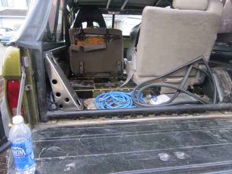 1974 Ford Bronco - The interior of a 1974 Ford Bronco shows its seats, a blue coiled hose, and a metal bracket in the cargo area.