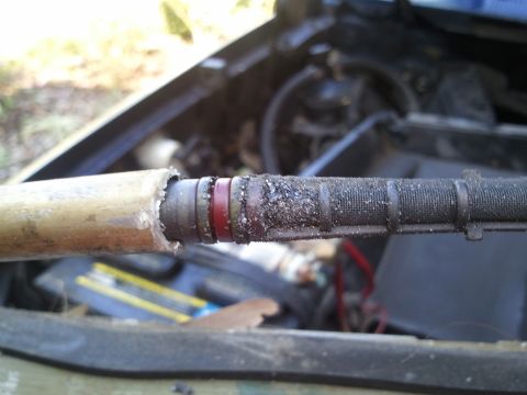 1994 Ford Bronco - Close-up of a worn automotive AC hose with visible damage and debris, set against an engine bay background.