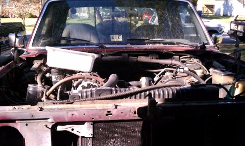 1979 Ford Bronco - The engine compartment of a red pickup truck is shown with various mechanical components exposed.
