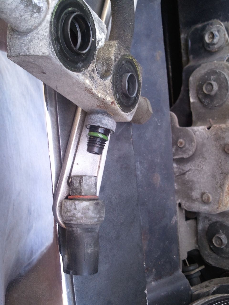 AC system part with green O-ring and hex bolt, attached to metal bracket