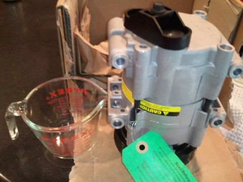 1994 Ford Bronco - An air conditioning compressor is shown next to a Pyrex measuring cup, with a green tag attached to the compressor.