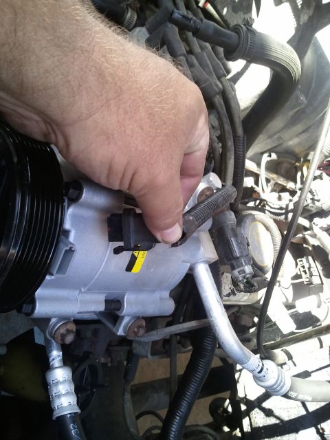 1994 Ford Bronco - A hand is shown connecting a wire to the AC compressor unit in an engine bay.
