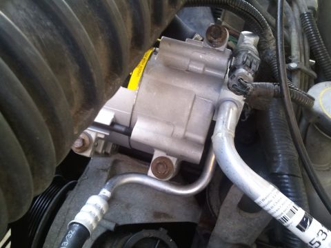 1994 Ford Bronco - Close-up view of an AC compressor and associated lines within an engine compartment. A yellow warning sticker is partially visible on the u…