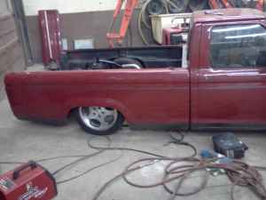1970 Ford Ranchero - A red pickup truck is shown from the side in a workshop, custom wheels and a lowered stance.