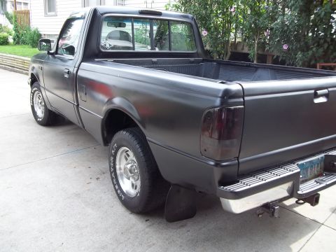 1970 Ford Ranchero - This black pickup truck is parked on a concrete driveway with trees in the background.