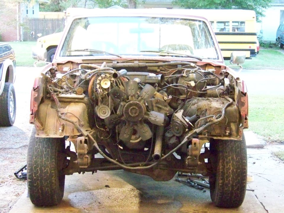 red pickup truck, front end removed showing engine and chassis components. Tires and suspension visible